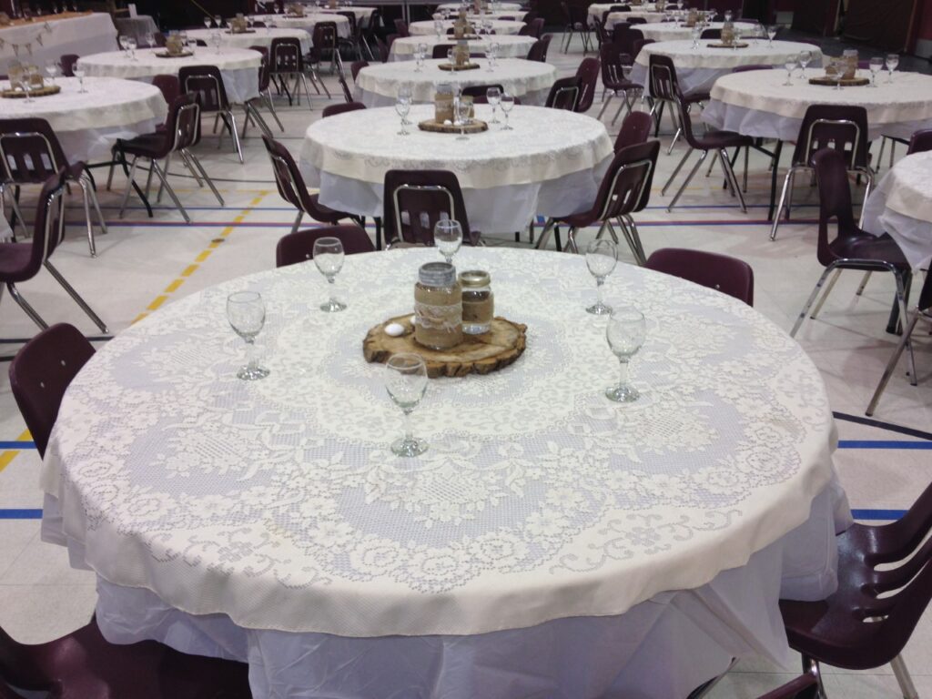 Many circular tables set up in the gym/hall with linen and dining ware.