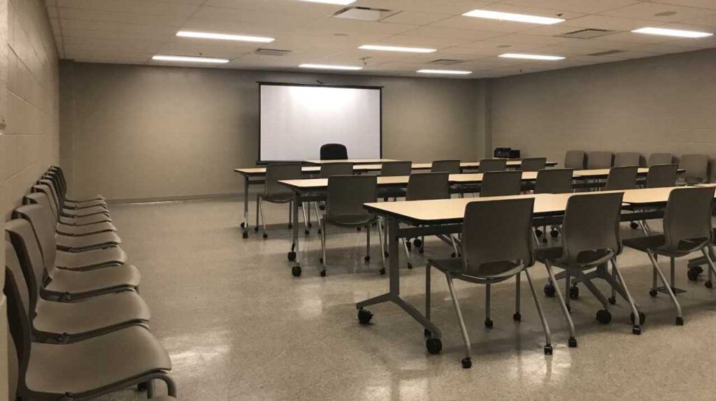 A clean, bare boardroom with tables, chairs and a projection screen/whiteboard set up.